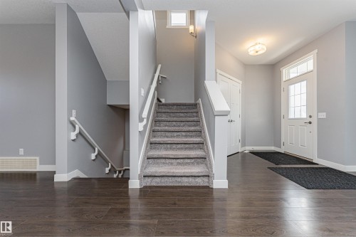 Entryway featuring wood-finish flooring, a carpeted staircase with white handrails, and a front door with decorative window inserts - 16420 15 Avenue, Edmonton, AB - Indoor Photo Showing Other Room