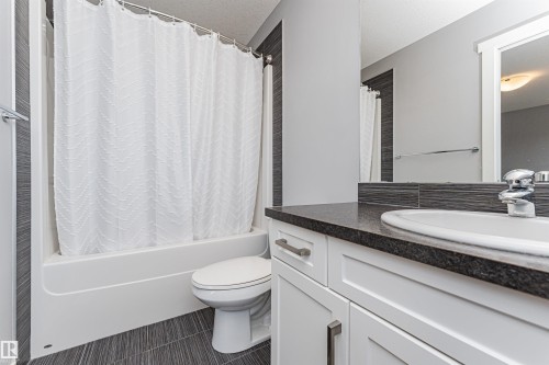 Bathroom featuring a white tub/shower combination, a white toilet, and dark grey tile flooring - 16420 15 Avenue, Edmonton, AB - Indoor Photo Showing Bathroom