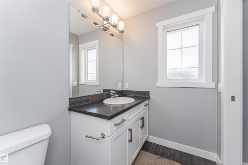 Bathroom vanity with a dark countertop, white cabinetry, and a rectangular undermount sink - 16420 15 Avenue, Edmonton, AB - Indoor Photo Showing Bathroom