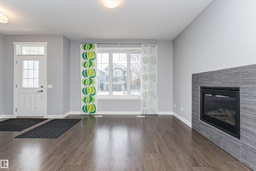 Spacious room featuring wood-finish flooring, a contemporary fireplace with stacked stone surround, and light gray wall color - 16420 15 Avenue, Edmonton, AB - Indoor Photo Showing Living Room With Fireplace