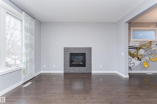 Living area featuring a floor-to-ceiling window, wood-finish flooring, and a fireplace with a stacked stone-look surround - 16420 15 Avenue, Edmonton, AB - Indoor With Fireplace