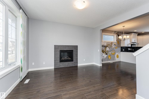 Spacious open-concept room featuring wood-finish flooring, a contemporary fireplace with a stacked stone surround, and large windows - 16420 15 Avenue, Edmonton, AB - Indoor Photo Showing Living Room With Fireplace