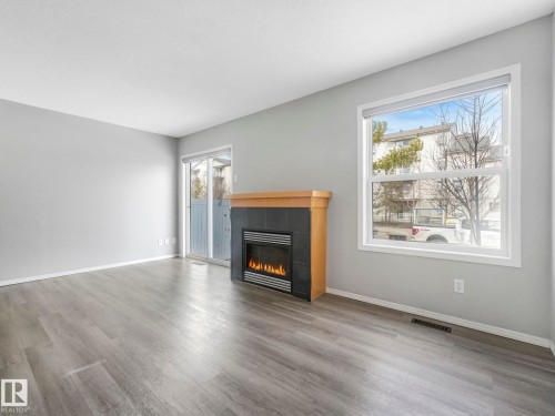 The property features a living area with light grey walls and grey wood-style flooring - 175 150 Edwards Drive, Edmonton, AB - Indoor Photo Showing Living Room With Fireplace