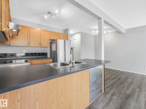 The kitchen features oak cabinetry, dark countertops, and a double basin stainless steel sink - 175 150 Edwards Drive, Edmonton, AB - Indoor Photo Showing Kitchen With Double Sink