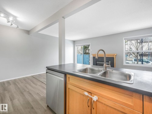 This kitchen features a double basin stainless steel sink with a gooseneck faucet, a stainless steel dishwasher, and wooden cabinetry with a dark countertop - 175 150 Edwards Drive, Edmonton, AB - Indoor Photo Showing Kitchen With Double Sink