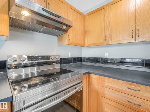 The kitchen features wood cabinetry, a stainless steel range with a smooth cooktop, and a matching stainless steel range hood - 175 150 Edwards Drive, Edmonton, AB - Indoor Photo Showing Kitchen