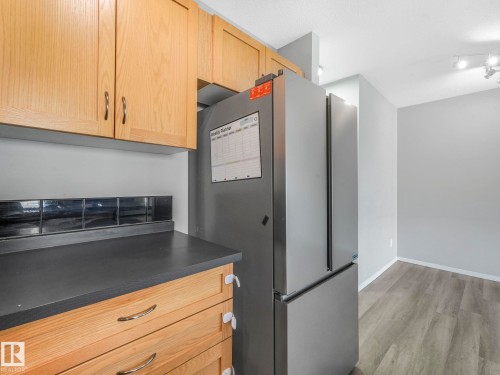Kitchen featuring light wood cabinetry, dark countertops, and a stainless steel refrigerator - 175 150 Edwards Drive, Edmonton, AB - Indoor