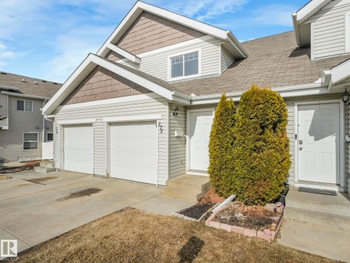 The property features a two-car garage with white doors, a light-colored siding exterior, and a shingled roof - 175 150 Edwards Drive, Edmonton, AB - Outdoor With Exterior