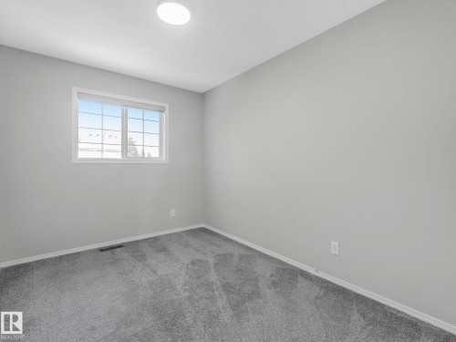 This room features gray carpet flooring, light gray walls, and a window with white framing and grilles - 175 150 Edwards Drive, Edmonton, AB - Indoor Photo Showing Other Room