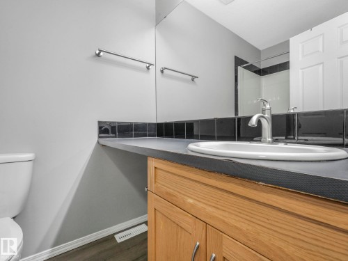 The bathroom features a vanity with a light wood base and a dark countertop, a white oval sink with a chrome faucet, and a large mirror - 175 150 Edwards Drive, Edmonton, AB - Indoor Photo Showing Bathroom