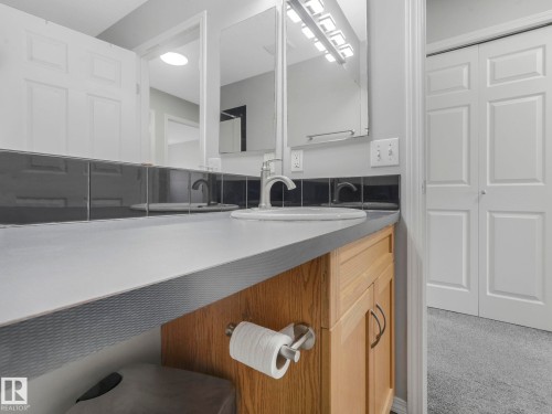 The bathroom features a light-colored countertop, a white sink with a chrome faucet, and a light-toned wooden vanity with cabinets and handles - 175 150 Edwards Drive, Edmonton, AB - Indoor