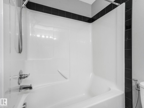 Bathroom featuring a white bathtub with a chrome faucet and shower head, complemented by a black tiled surround - 175 150 Edwards Drive, Edmonton, AB - Indoor Photo Showing Bathroom