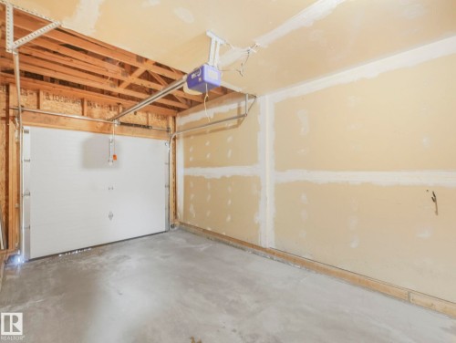 The property includes a garage with a concrete floor, exposed ceiling joists, and a white overhead door - 175 150 Edwards Drive, Edmonton, AB - Indoor Photo Showing Garage