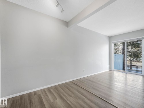 Living area featuring light-colored walls, wood-style flooring, track lighting, and a large sliding glass door - 175 150 Edwards Drive, Edmonton, AB - Indoor Photo Showing Other Room