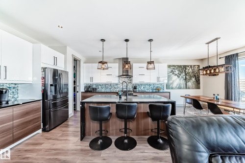 Open-concept kitchen featuring an oversized island with a dark countertop and three pendant lights, two-tone cabinetry, a mosaic tile backsplash, and wood-finish flooring - 5263 47 Ave, Calmar, AB - Indoor Photo Showing Kitchen With Upgraded Kitchen