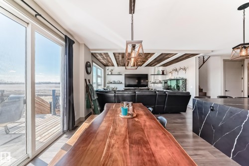 Open-concept living space featuring wood-finish flooring, a large sliding glass door opening to an outdoor deck, a kitchen island with a dark stone countertop, and decorative ceiling beams - 5263 47 Ave, Calmar, AB - Indoor Photo Showing Dining Room