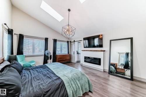 Vaulted ceiling with skylights, featuring an integrated linear electric fireplace with a rustic wood mantel, two window units, and wood-finish flooring - 5263 47 Ave, Calmar, AB - Indoor Photo Showing Bedroom With Fireplace