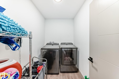 Dedicated laundry area featuring a washer and dryer set, wood-finish flooring, and a modern interior door with a black handle - 5263 47 Ave, Calmar, AB - Indoor Photo Showing Laundry Room