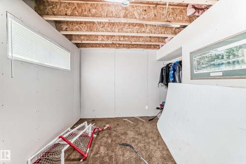 Partially finished room featuring exposed ceiling joists and subfloor, gypsum board walls, a horizontal window with blinds, and an open closet space - 5263 47 Ave, Calmar, AB - Indoor Photo Showing Other Room