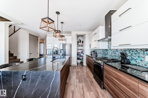 Gourmet kitchen featuring a waterfall island with a double basin sink, wood-finish flooring, full height backsplash, stainless steel appliances, and a pantry with built-in shelving - 5263 47 Ave, Calmar, AB - Indoor Photo Showing Kitchen