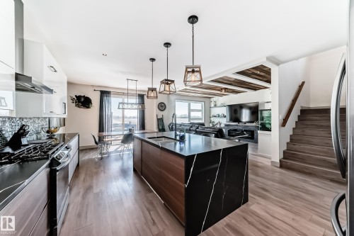 Gourmet kitchen featuring a large waterfall island with a black and white veined countertop, pendant lighting, wood-finish flooring, and a dining area with expansive windows - 5263 47 Ave, Calmar, AB - Indoor Photo Showing Kitchen With Upgraded Kitchen