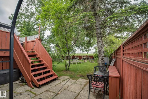 Expansive rear yard featuring a wooden deck with staircase, mature trees, a manicured lawn, and concrete paver patio - 4823 10 Avenue, Edmonton, AB 