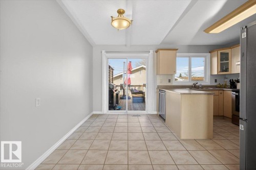 Kitchen and dining area featuring tile flooring, light wood-finish cabinetry, a window above the sink, and a sliding glass door opening to an outdoor deck - 13508 81 Street, Edmonton, AB - Indoor Photo Showing Kitchen