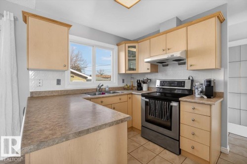 Kitchen featuring light wood-finish cabinetry, tile flooring, a built-in stainless steel range, and a dual basin sink with a window overhead - 13508 81 Street, Edmonton, AB - Indoor Photo Showing Kitchen With Double Sink