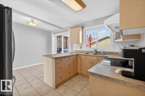 Kitchen featuring light wood-finish cabinetry, a ceramic tile backsplash, and a double-basin stainless steel sink - 13508 81 Street, Edmonton, AB - Indoor Photo Showing Kitchen With Double Sink