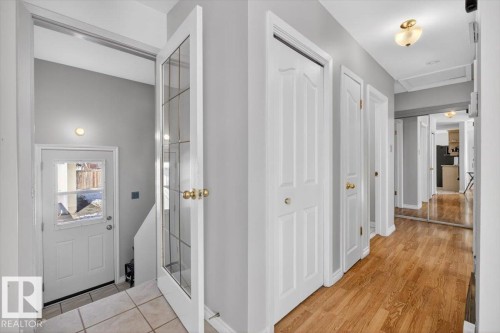 Hallway featuring wood-finish flooring, white paneled doors with brass hardware, and a mirrored wall - 13508 81 Street, Edmonton, AB - Indoor Photo Showing Other Room