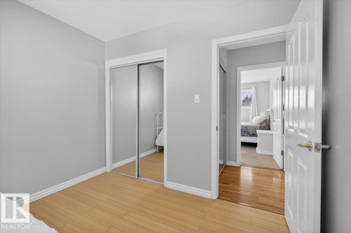 Room featuring wood-finish flooring, light gray walls, white trim, and a mirrored sliding closet door - 13508 81 Street, Edmonton, AB - Indoor Photo Showing Other Room