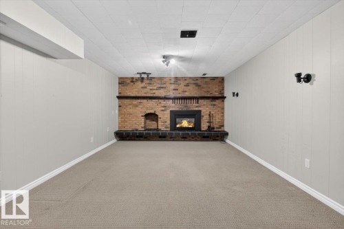Carpeted room featuring a brick fireplace with a black wood-burning insert and a tiled hearth - 13508 81 Street, Edmonton, AB - Indoor With Fireplace