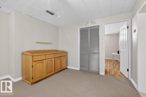 Carpeted room featuring a built-in wooden cabinet with multiple drawers and doors, a small floating shelf, and a louvered bi-fold closet - 13508 81 Street, Edmonton, AB - Indoor