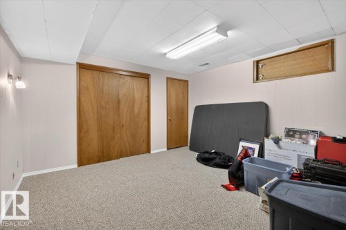 Carpeted room featuring wood-finish bi-fold closet doors, a panel-style door, and a drop ceiling with fluorescent lighting - 13508 81 Street, Edmonton, AB - Indoor