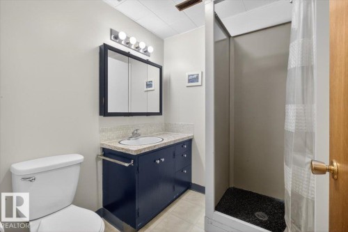 Bathroom featuring a blue vanity with an integrated sink, a light-toned countertop, and a mirrored medicine cabinet with overhead lighting - 13508 81 Street, Edmonton, AB - Indoor Photo Showing Bathroom