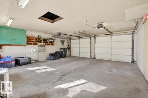 Two-car garage featuring a concrete floor, two individual garage doors with openers, built-in cabinetry, and overhead fluorescent lighting - 13508 81 Street, Edmonton, AB - Indoor Photo Showing Garage