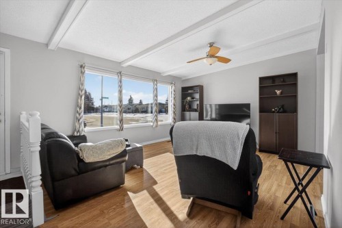 Bright living area featuring wood-finish flooring, a white ceiling with exposed beams, and a ceiling fan with integrated lighting - 13508 81 Street, Edmonton, AB - Indoor