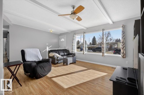Bright living area featuring wood-finish flooring, a white-painted ceiling with exposed beams, and a ceiling fan with integrated lighting - 13508 81 Street, Edmonton, AB - Indoor Photo Showing Living Room