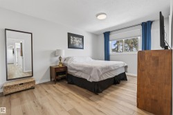 Bedroom featuring light wood-finish flooring, a contemporary ceiling light fixture, a window with a roller shade, and a full-length wall mirror - 