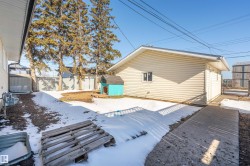 Rear exterior featuring a detached structure with siding, a concrete pathway, a metal gate, and mature evergreen trees - 