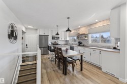 Modern kitchen featuring white cabinetry, stainless steel appliances, wood-finish flooring, and a brick-look accent wall - 