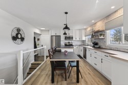 Bright kitchen featuring white cabinetry, stainless steel appliances, wood-finish countertops, and a distressed brick-style backsplash - 