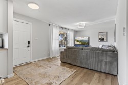 Open living area featuring wood-finish flooring, light grey walls, a white entry door with matte black hardware, and an overhead flush-mount light fixture - 