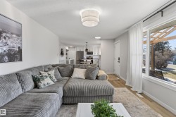 Bright living area featuring wood-finish flooring, a contemporary ceiling light fixture, and large window with white trim - 