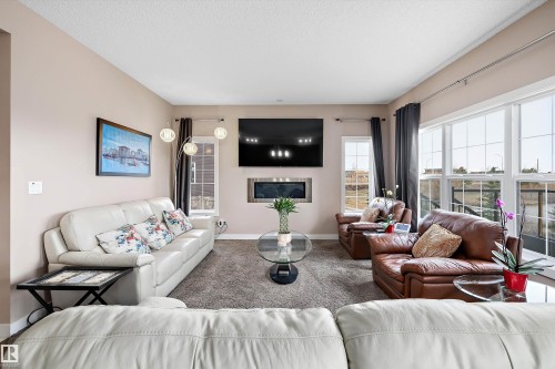 Spacious living area featuring expansive windows, neutral wall tones, a built-in electric fireplace, and textured carpet flooring - 1586 Chapman Way, Edmonton, AB - Indoor Photo Showing Living Room With Fireplace
