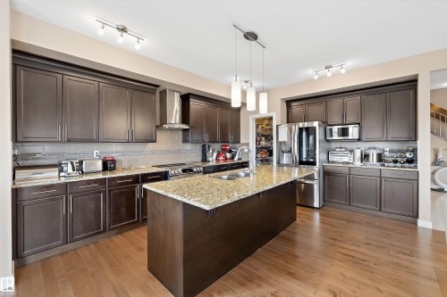 Kitchen featuring dark wood-finish cabinetry, stainless steel appliances, a tile backsplash, and a central island with a granite countertop and pendant lighting - 1586 Chapman Way, Edmonton, AB - Indoor Photo Showing Kitchen With Double Sink With Upgraded Kitchen