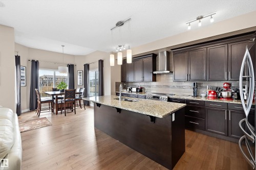 Kitchen with dark wood cabinetry, light-toned wood-finish flooring, and a central island featuring a speckled countertop - 1586 Chapman Way, Edmonton, AB - Indoor Photo Showing Kitchen With Upgraded Kitchen