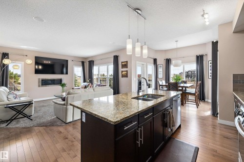 Open-concept living area featuring a kitchen island with stone countertop, stainless steel sink, and pendant lighting - 1586 Chapman Way, Edmonton, AB - Indoor Photo Showing Other Room With Fireplace