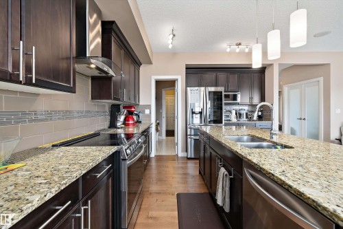 Modern kitchen featuring dark wood cabinetry, light-toned granite countertops, and stainless steel appliances - 1586 Chapman Way, Edmonton, AB - Indoor Photo Showing Kitchen With Double Sink With Upgraded Kitchen