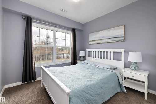 Bright bedroom featuring a large window with grid panes, textured grey carpeting, light purple walls, and white trim - 1586 Chapman Way, Edmonton, AB - Indoor Photo Showing Bedroom